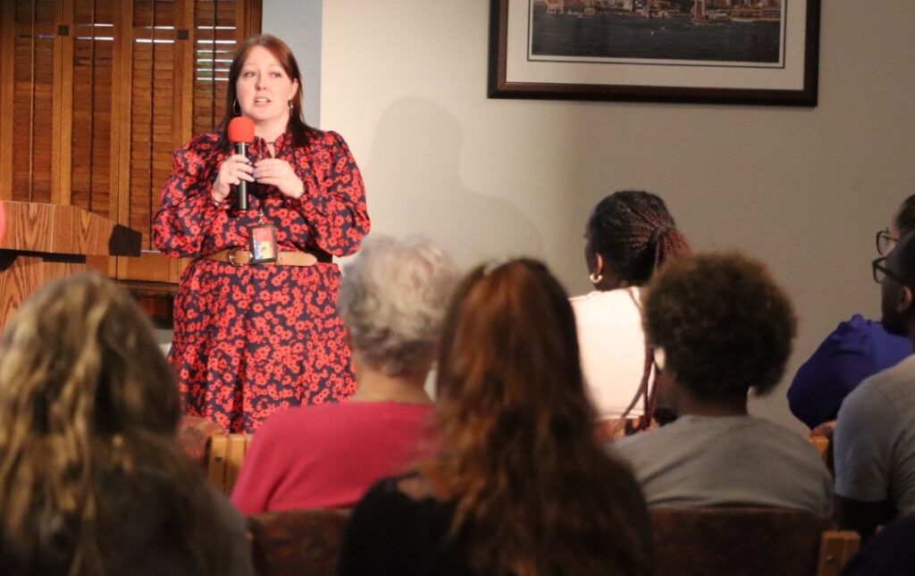 Laura in a red dress as she speaks to a crowd of individuals.